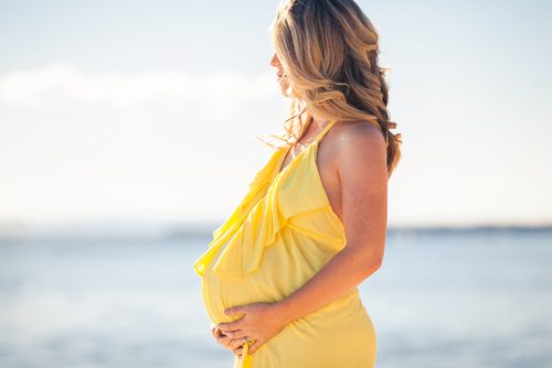 Profile of a pregnant woman in yellow dress holding her belly
